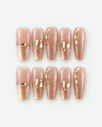Champagne shimmer long coffin press-on nails with glossy nude sections and sculptural gold jewellery accents
